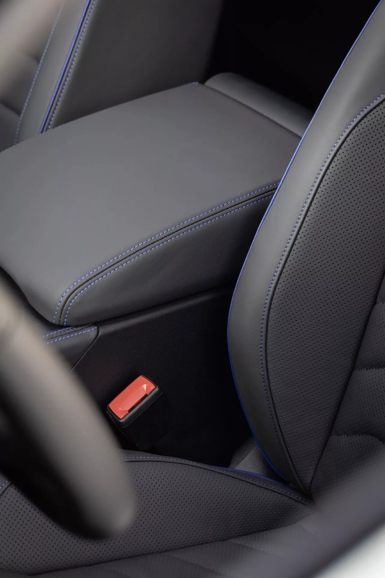 Vue détaillée de l'intérieur du VW Touareg (III facelift) 2023 montrant la conception ergonomique d'un siège en cuir noir avec coutures contrastées, centre perforé pour le potentiel chauffage/refroidissement, et une boucle de ceinture de sécurité rouge mettant en évidence les caractéristiques de luxe et de sécurité