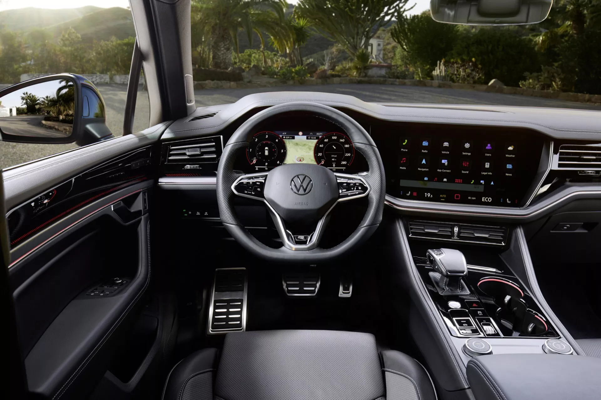 Vue intérieure du Volkswagen Touareg 2023 depuis le siège conducteur montrant un volant moderne à trois branches avec le logo Volkswagen, un tableau de bord numérique, un système d'infodivertissement à écran tactile large sur le tableau de bord, un minimum de commandes physiques, un levier de vitesses automatique et des sièges en cuir premium avec commandes visibles